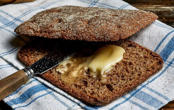 Two pieces of rye bread on a kitchen towel. There is melted butter on the bread and a knife.