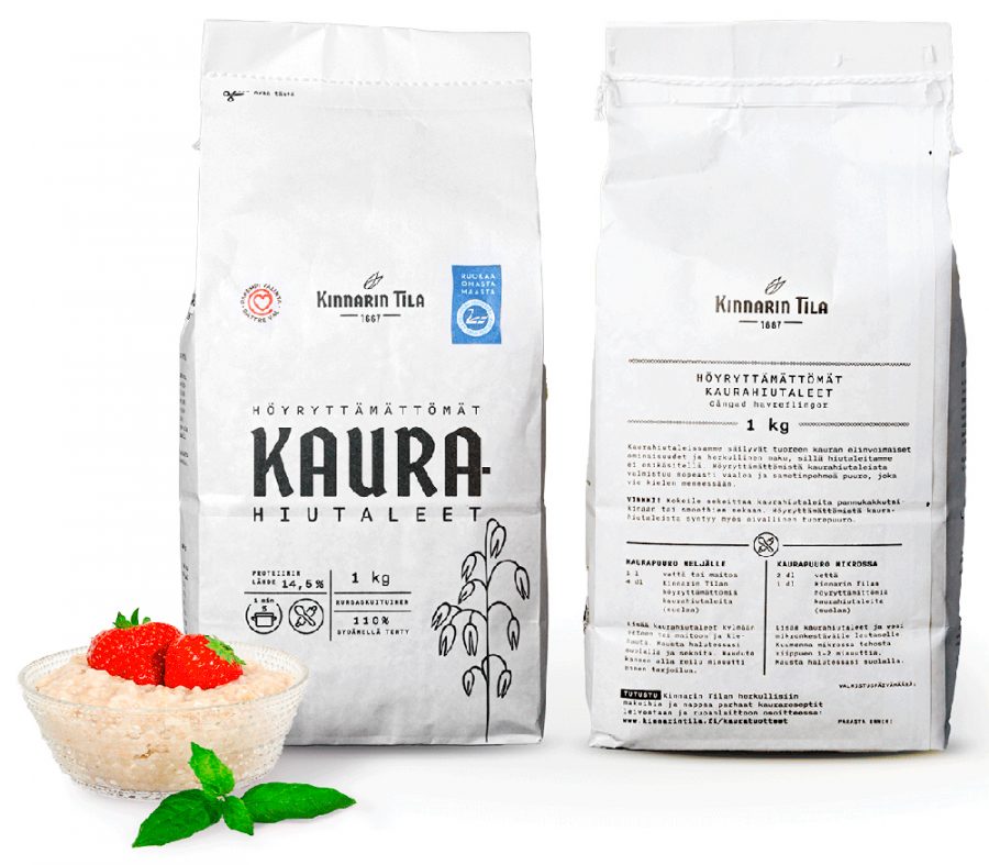 Two bags of Kinnarin Farm oat flakes on the table, a cup of porridge decorated with strawberries.